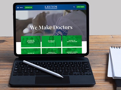 LECOM.edu website on tablet laptop on wooden desk with notebooks and pens surrounding.
